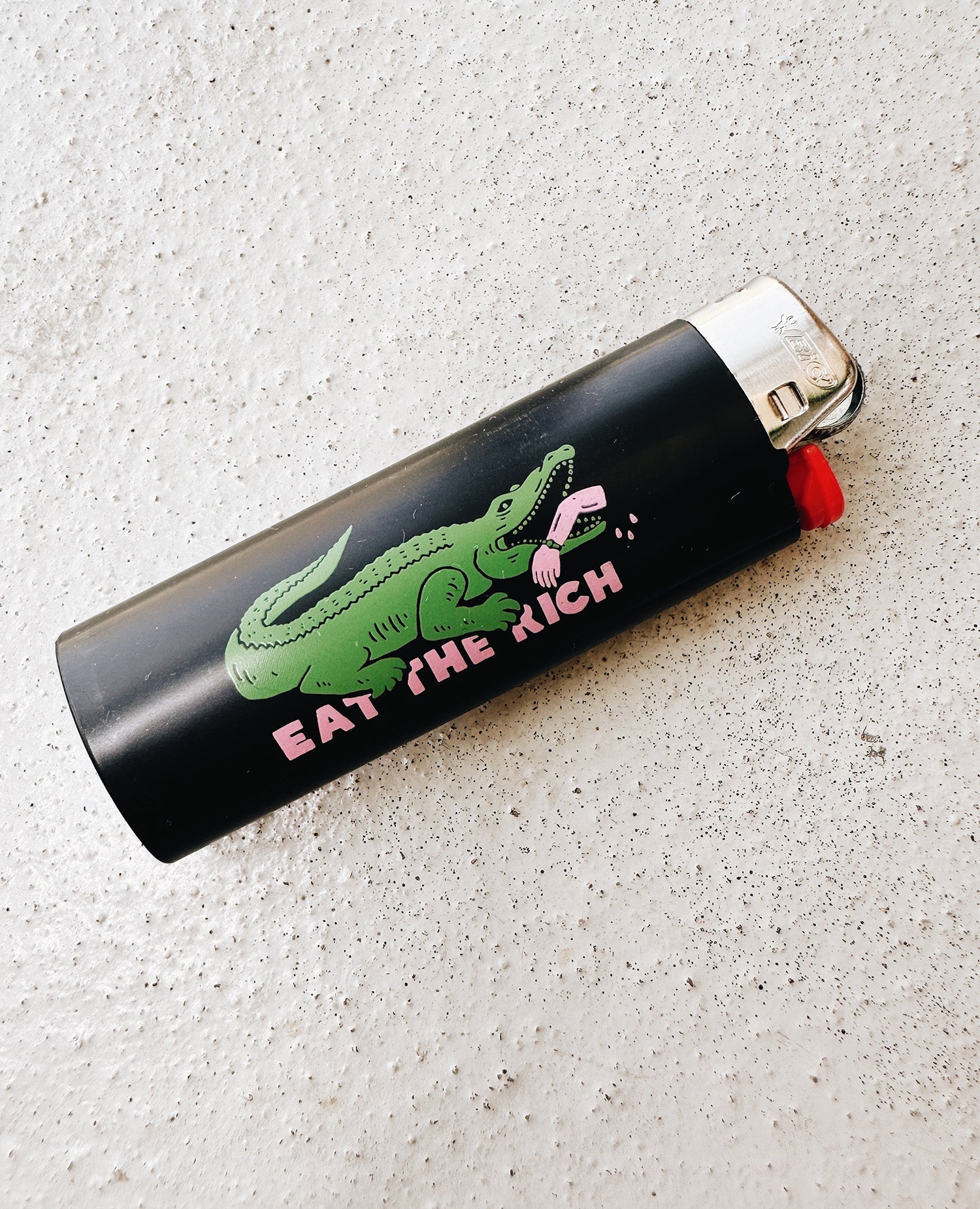 Eat The Rich Feuerzeug Schwarz von NKSP – Alligator-Print mit Statement-Schriftzug