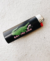 Eat The Rich Feuerzeug Schwarz von NKSP – Alligator-Print mit Statement-Schriftzug