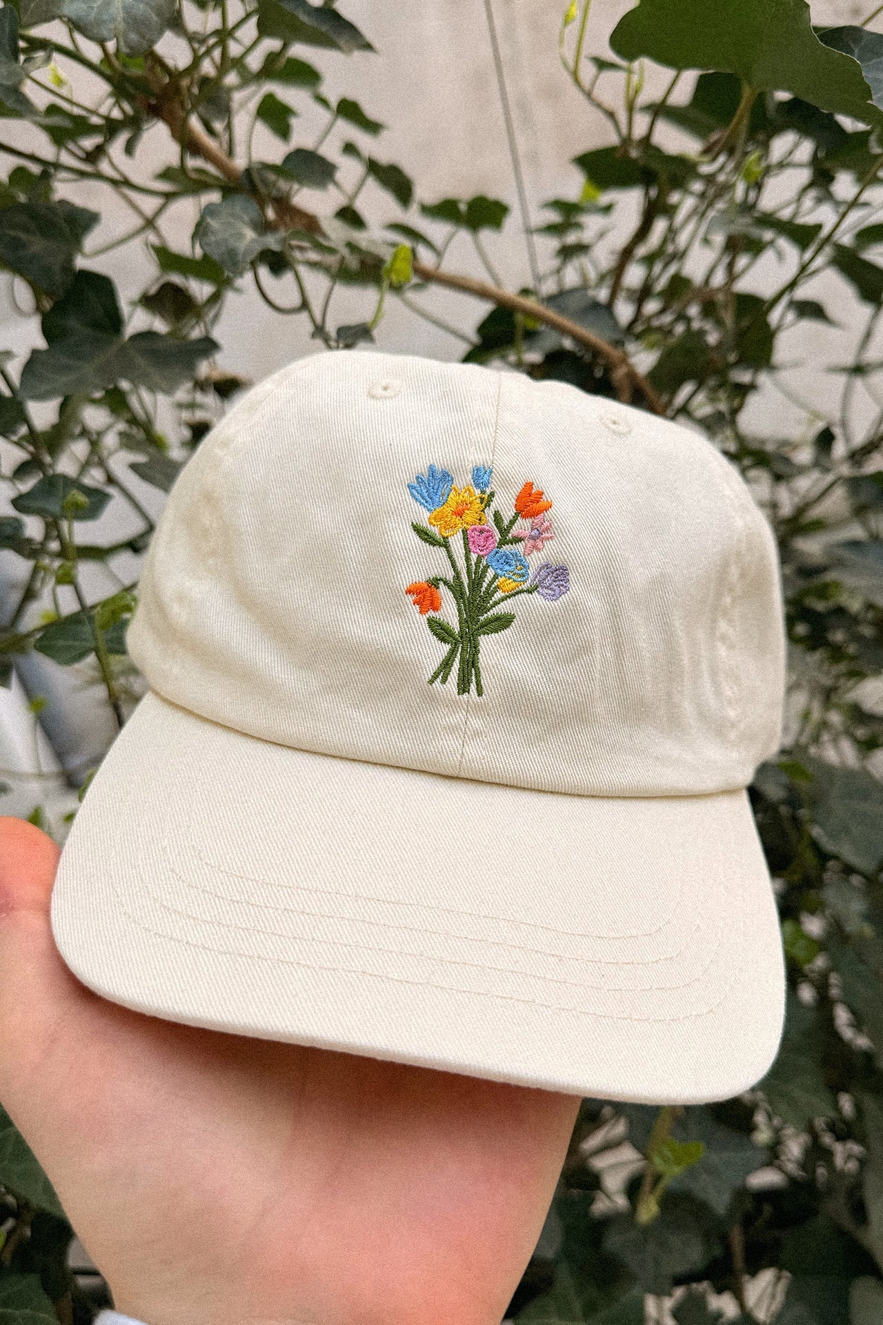 Wien Streetwear Dad Cap in Creme mit bunter Blumenstrauß-Stickerei, Seitenansicht auf Hand gehalten
