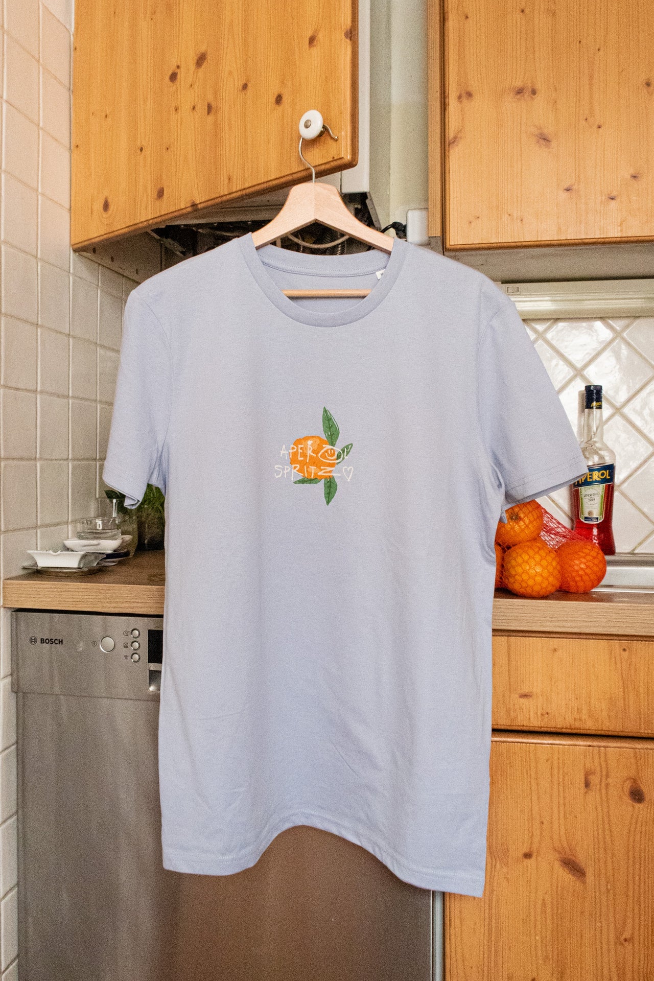 Aperol Spritz T-Shirt hellblau Vorderseite, kleine Orangen-Illustration mit Schriftzug auf Brust, Straight Fit