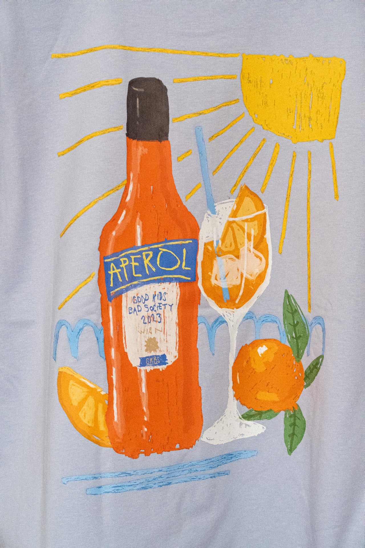 Detailaufnahme Rückenprint: Aperol-Flasche, Spritz-Glas und Sonne auf hellblauem Bio Baumwolle T-Shirt, GKBS Wien