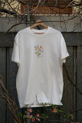 Off White Loose Fit T-Shirt Vorderseite, kleiner bunter Blumenstrauß-Print mit GKBS Schriftzug, Bio Baumwolle Wien