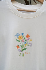 Nahaufnahme bunter Blumenstrauß-Print auf Off White Bio Baumwolle T-Shirt, GKBS Schriftzug, Rundhals Größe M sichtbar